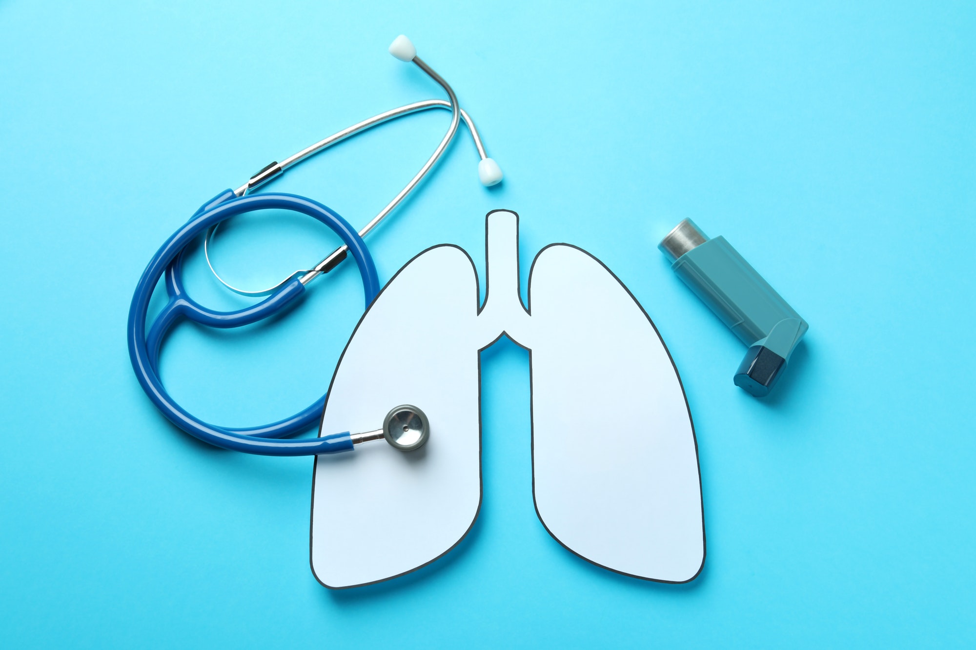 Decorative lungs, stethoscope and inhaler on blue background